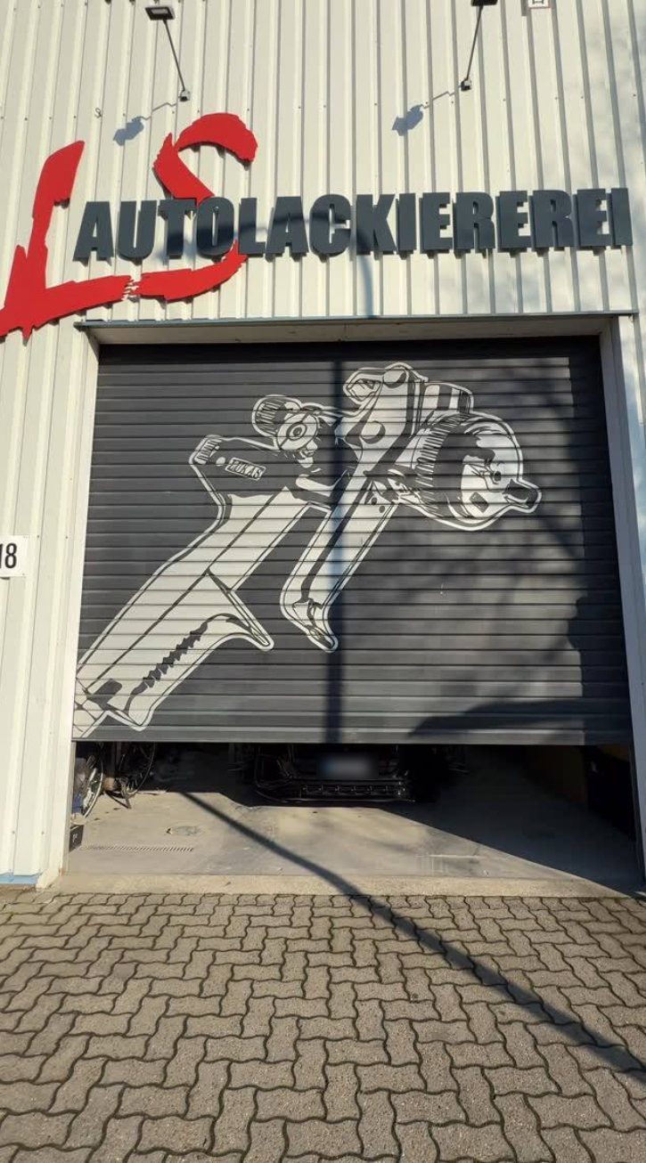 Rolltor der Werkstatt mit großer Lackierpistole als Wandbild, darüber das LS-Logo