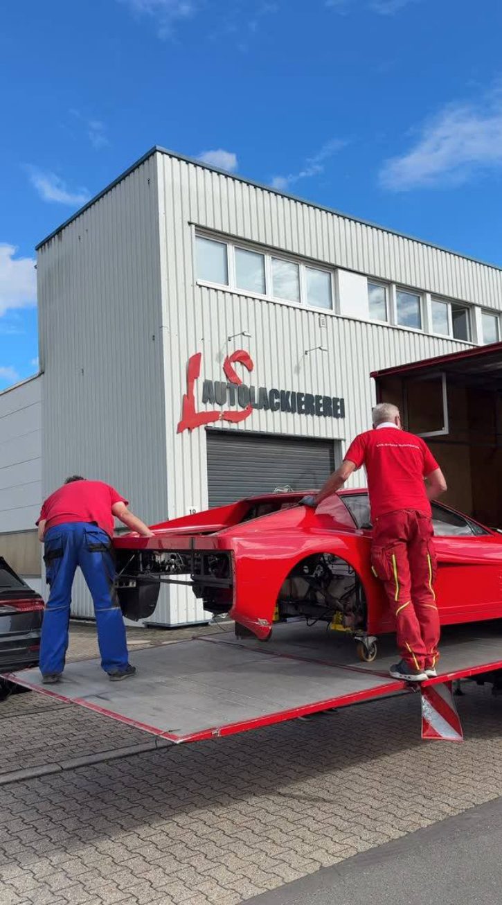 Roter Ferrari wird vor der Werkstatt vom Anhänger geladen